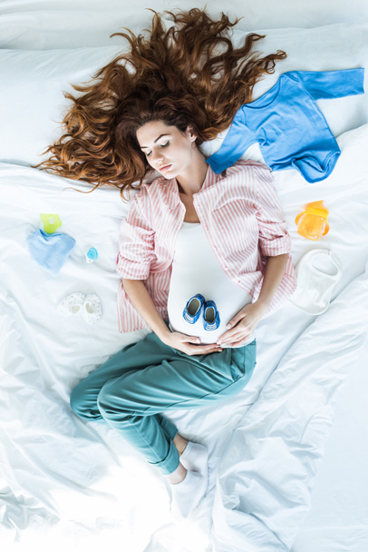 Bovenaanzicht van zwangere vrouw in bed slapen onder de kleren van de baby - Foto, afbeelding