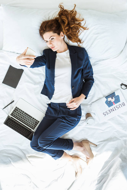 Top view of businesswoman in suit taking selfie in bed among folders and documents - Foto, Imagem