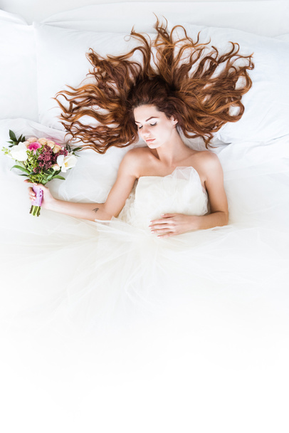 Vista superior de la novia con vestido blanco durmiendo en la cama con ramo de flores
 - Foto, imagen