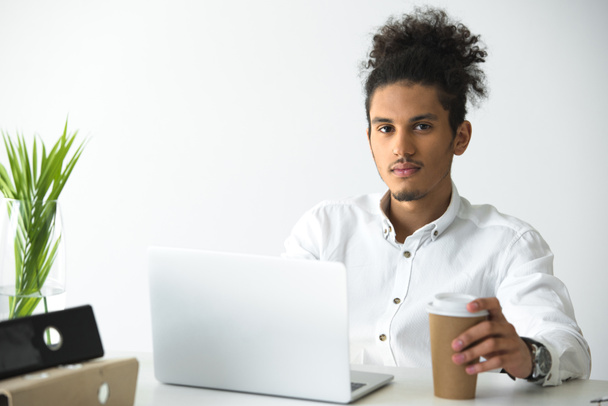 komea nuori afrikkalainen amerikkalainen liikemies käyttää kannettavaa tietokonetta ja katselee kameraa
 - Valokuva, kuva
