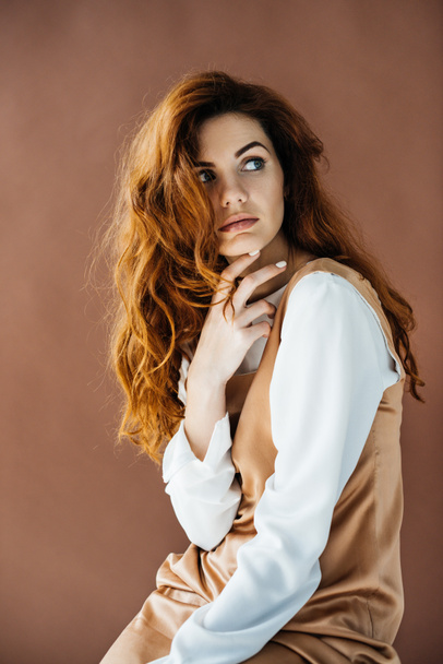 Woman with long red hair posing with hand near face isolated on brown background - Foto, immagini