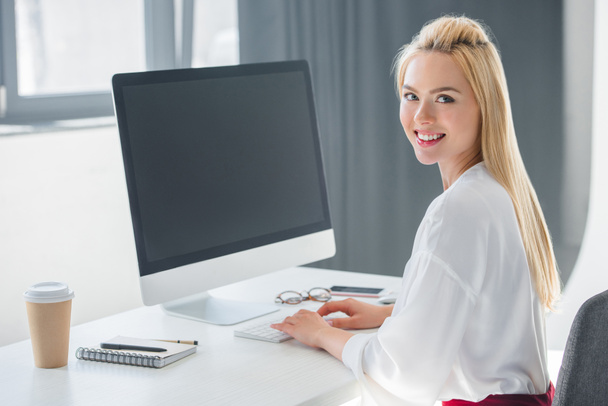 belle jeune femme d'affaires souriant à la caméra tout en travaillant avec ordinateur de bureau dans le bureau
 - Photo, image