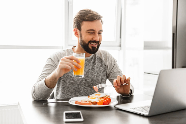 Optimistic adult man 30s wearing casual clothing eating fried eg - Photo, image