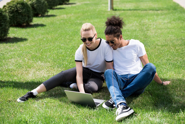 happy young multiethnic couple sitting on grass and using laptop - Valokuva, kuva