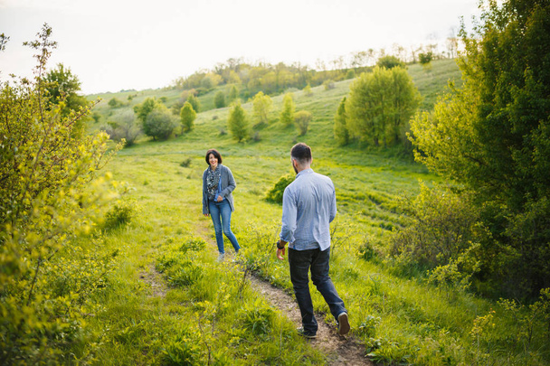 手徒歩春夕焼けの田園地帯の牧草地を保持している美しい若いカップル - 写真・画像