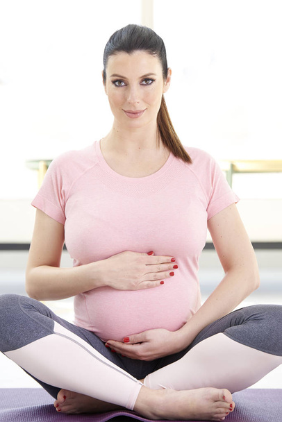 pregnant young woman sitting in lotus pose doing yoga at home - Photo, Image