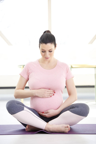 pregnant young woman sitting in lotus pose doing yoga at home - Photo, image