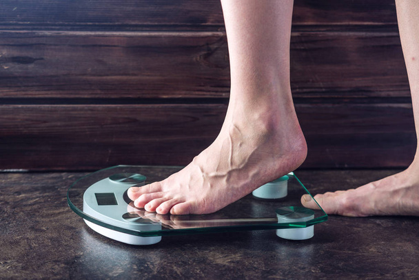 Frauenfüße stehen auf elektronischen Waagen zur Gewichtskontrolle auf dunklem Hintergrund. Konzept des Sporttrainings, Ernährung - Foto, Bild