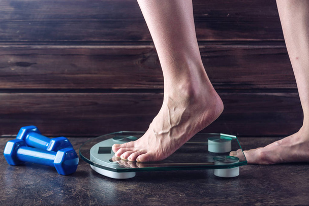 Γυναικεία πόδια καθώς στέκεται όρθιος στην ηλεκτρονική ζυγαριά για έλεγχο του βάρους σε σκούρο φόντο. Έννοια της αθλητική προπόνηση, δίαιτες - Φωτογραφία, εικόνα