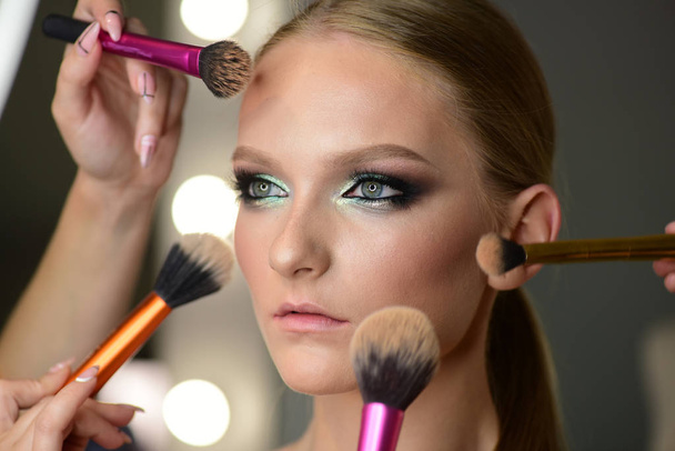 Beautiful young woman with makeup brushes around face - Photo, image