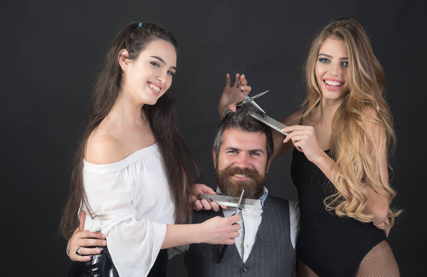 Closeup view of young beautiful people of beautiful fashionable female barber cutting and holding scissors and handsome man with long beard in studio - Fotografie, Obrázek