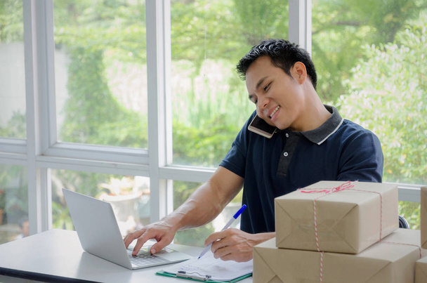Start up. young man happy after new order from customer with laptop, mobile phone and delivery packaging box on table, small business owner working at home office, SME, shopping online concept - Foto, imagen