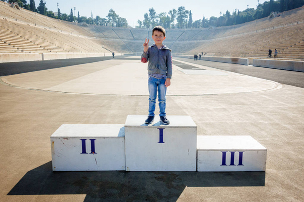 Niño posando en el podio del ganador en el Panathinaiko Stadium, Atenas, Grecia, Europa
 - Foto, Imagen