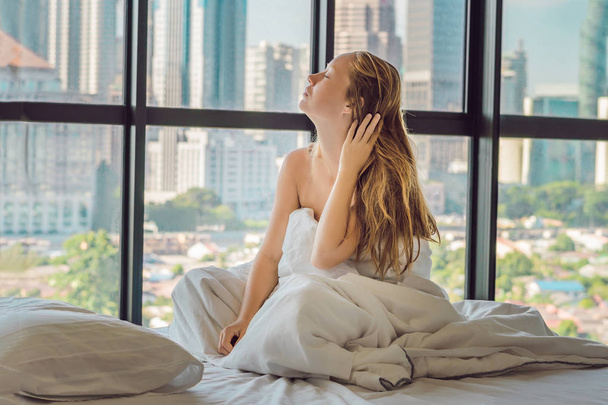 Young woman waking up in morning in apartment in downtown area with view of the skyscrapers. Life in noise of big city concept. Not enough sleep. - Фото, зображення