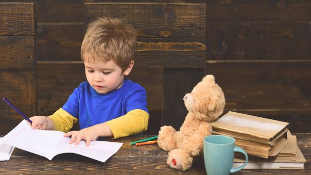 Concentrated kid writing in copybook. Preschool boy sitting at desk. Learning letters in kindergarten. - Zdjęcie, obraz