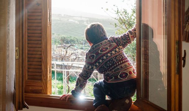 Vista trasera del niño sentado en la ventana de la casa, Grecia
 - Foto, Imagen