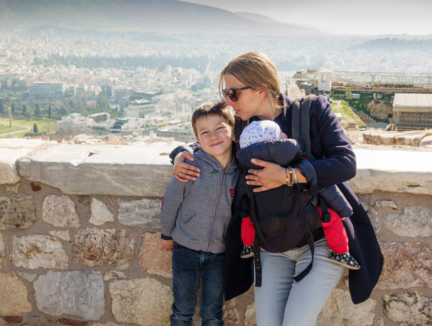 Mãe e filhos olhando para a câmera com a cidade de Atenas no pano de fundo, Grécia
 - Foto, Imagem