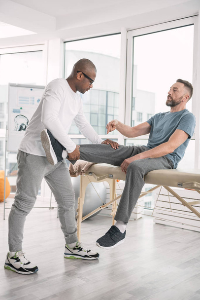 Nice professional therapist holding patients leg - Фото, зображення