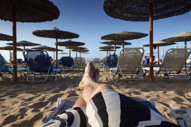 Sección baja de hombre descalzo relajante en silla de salón de playa de arena
 - Foto, Imagen