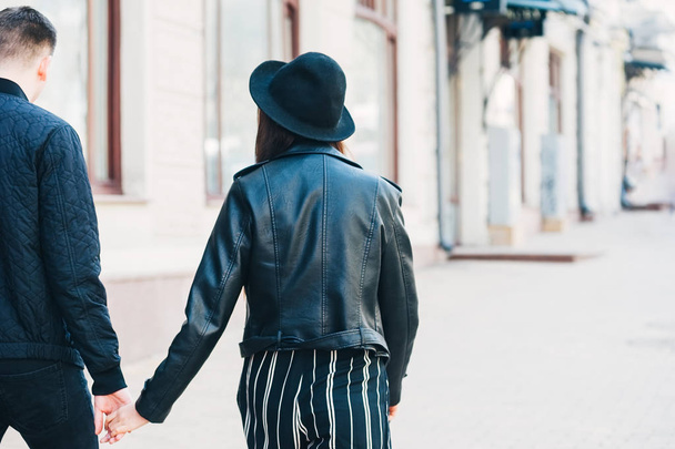 arkadan görünüşü siyah ceket, el ele tutuşarak genç bir çift - Fotoğraf, Görsel
