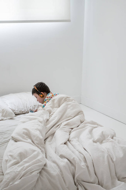 Мальчик слушает музыку на наушниках в постели
 - Фото, изображение