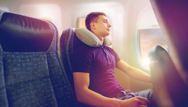 young man sleeping in plane with travel pillow - Foto, imagen