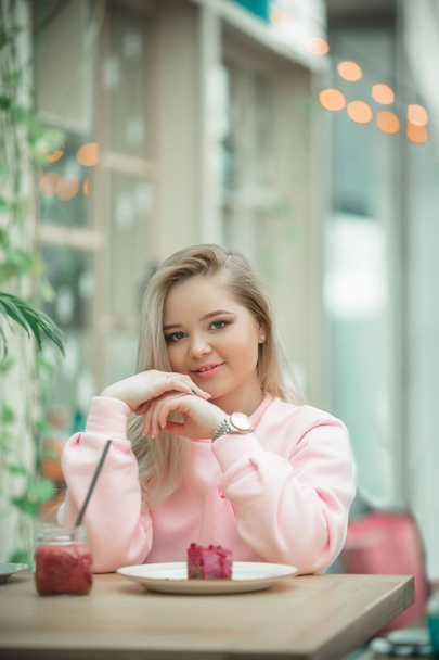 Pretty blonde girl is sitting on veranda in cafe and drinking red juice - Fotó, kép