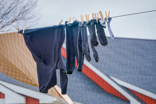 Outdoor view of clothes of Amish drying in the sun and air after laundry with a wooden red house background in Lancaster - 写真・画像