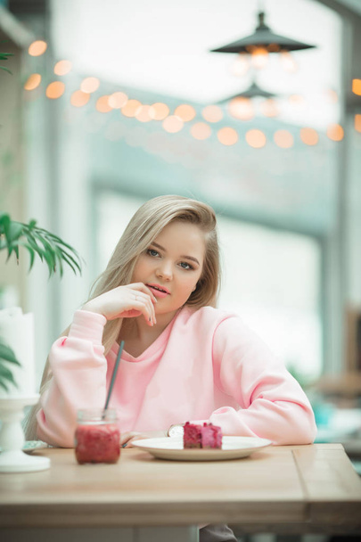 Cute young blonde girl is sitting on veranda in cafe and having nice breakfast - Фото, зображення