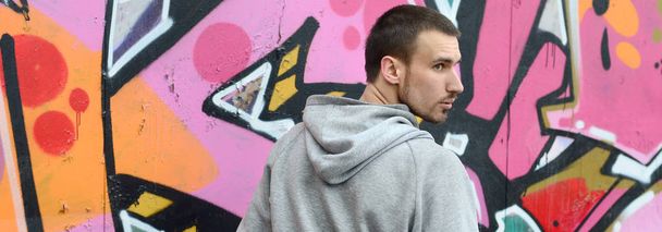 Un joven artista de graffiti mira a su alrededor mientras dibuja. Vándalo trata de no ser detectado mientras dibuja la imagen en la pared. El concepto de vandalismo y daño a la propiedad
 - Foto, Imagen