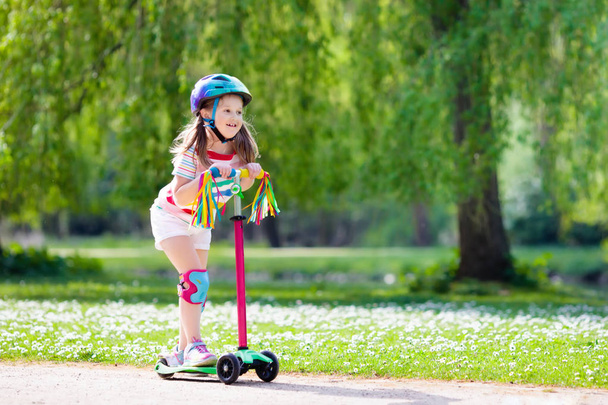 Child riding kick scooter in summer park. - Фото, зображення