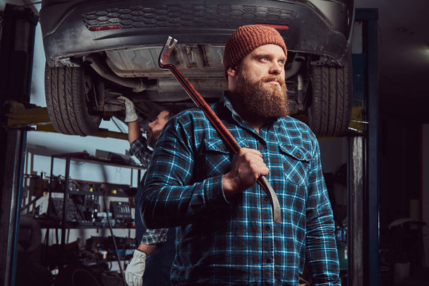 Two bearded brutal mechanics repair a car on a lift in the garage.  - Fotografie, Obrázek
