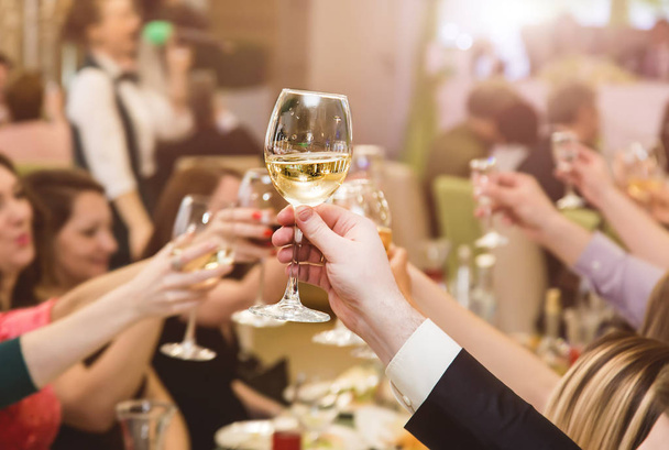 people at the table at a solemn event clink glasses and celebrate. A glass in a man's hand closeup - Foto, Imagem