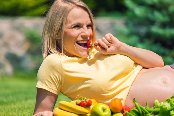 Pregnant woman lies on the grass and eats strawberries - Foto, Bild