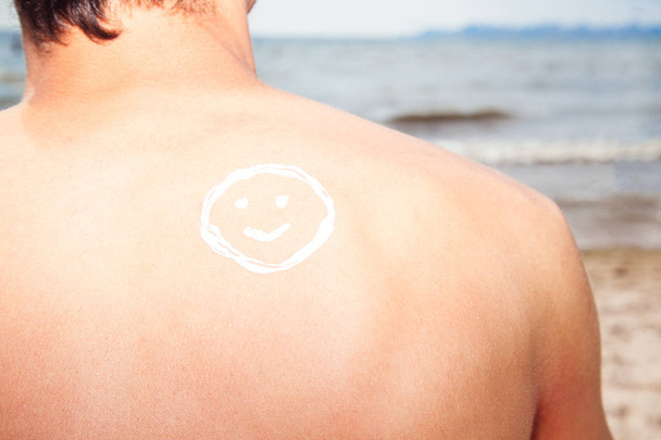 Lotion man met zonnebrandcrème smiley boven zee achtergrond - Foto, afbeelding
