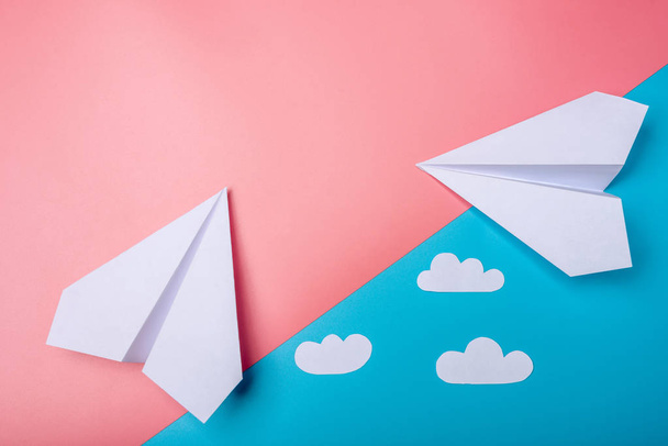 Witte papieren origami vliegtuigje met wolken ligt op pastel blauwe achtergrond, bovenaanzicht. - Foto, afbeelding