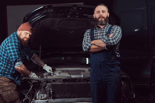 Service station. Two bearded brutal mechanics repairing a car in the garage. - Фото, изображение
