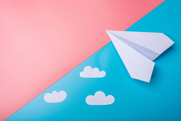 Белый бумажный оригами самолет с облаками лежит на пастельно-голубом фоне, вид сверху
. - Фото, изображение