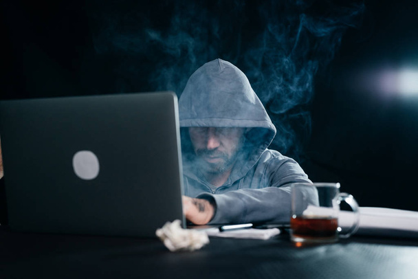 mysterious criminal man with a hood on his head hacking a laptop in the dark - Φωτογραφία, εικόνα