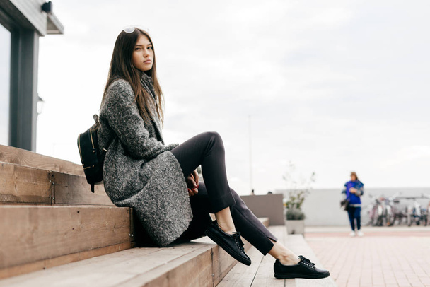 dark haired city girl posing outdoors in trendy gray coat, street style - 写真・画像