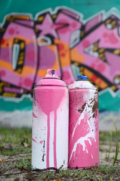 Kilka puszek farby używane leżeć na ziemi w pobliżu ściany z malowaniem graffiti piękne różowe i zielone kolory. Koncepcja sztuki ulicznej - Zdjęcie, obraz