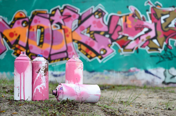 A few used paint cans lie on the ground near the wall with a beautiful graffiti painting in pink and green colors. Street art concept - Foto, imagen