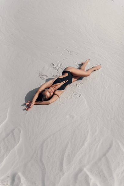 Attractive beautiful girl with perfect tanned fitness body lying on the sandy beach.Top view. - 写真・画像