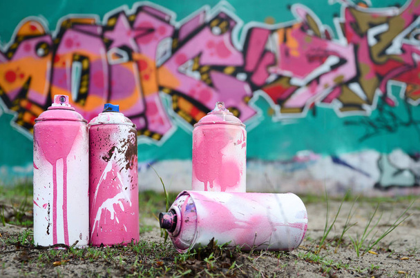 A few used paint cans lie on the ground near the wall with a beautiful graffiti painting in pink and green colors. Street art concept - Photo, Image