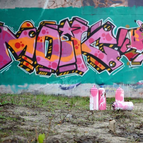 Kilka puszek farby używane leżeć na ziemi w pobliżu ściany z malowaniem graffiti piękne różowe i zielone kolory. Koncepcja sztuki ulicznej - Zdjęcie, obraz