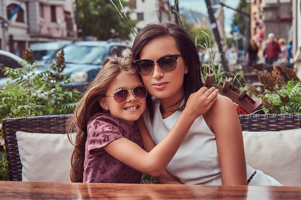 Portrait of fashionable mom and her lovely daughter during a time in an outdoor cafe. - Photo, Image