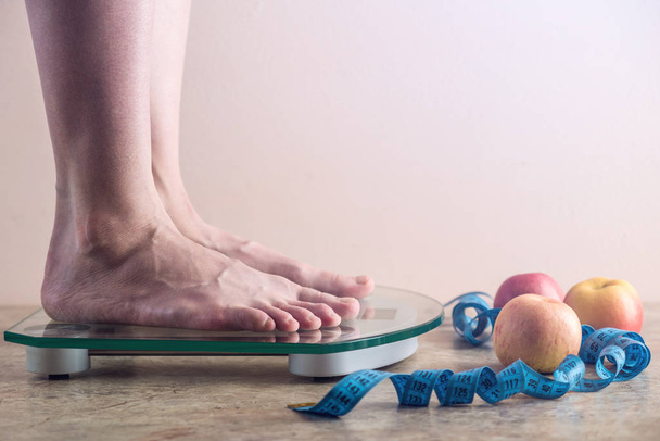 Kobiece nogi stojąc na wagi elektroniczne, do kontroli masy ciała z pomiaru taśmy i jabłka na jasnym tle. Koncepcja treningu, diety i odchudzanie sportowego - Zdjęcie, obraz