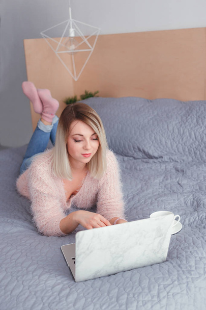 Happy casual beautiful woman working on a laptop lying on the bed in the hous - Foto, immagini
