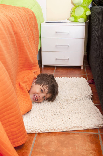Leikkisä lapsi piileskelee sängyn alla kotona
 - Valokuva, kuva