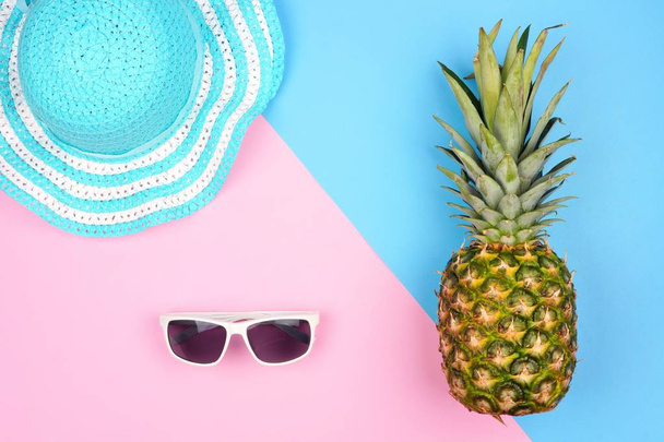 Pineapple with summer fashion accessories. Top view against a pink and blue background. - Photo, Image
